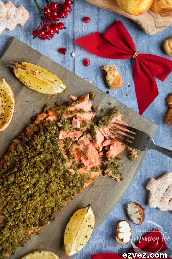 Overhead of salmon on wooden board, with a fork breaking into the filet and holiday trimmings like a red bow, star fruit and fake berries nearby.