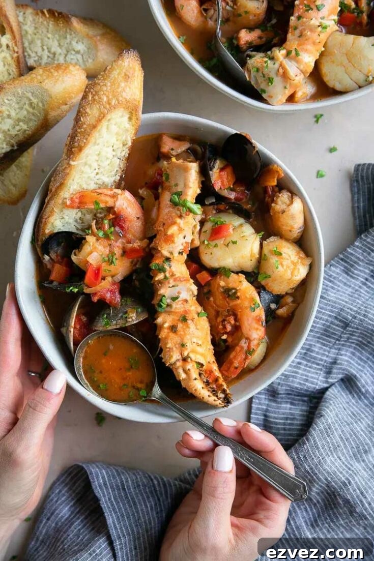 Overhead of finished recipe in white bowl with hands dipping broth on a spoon and a second bowl and pieces of bread nearby.