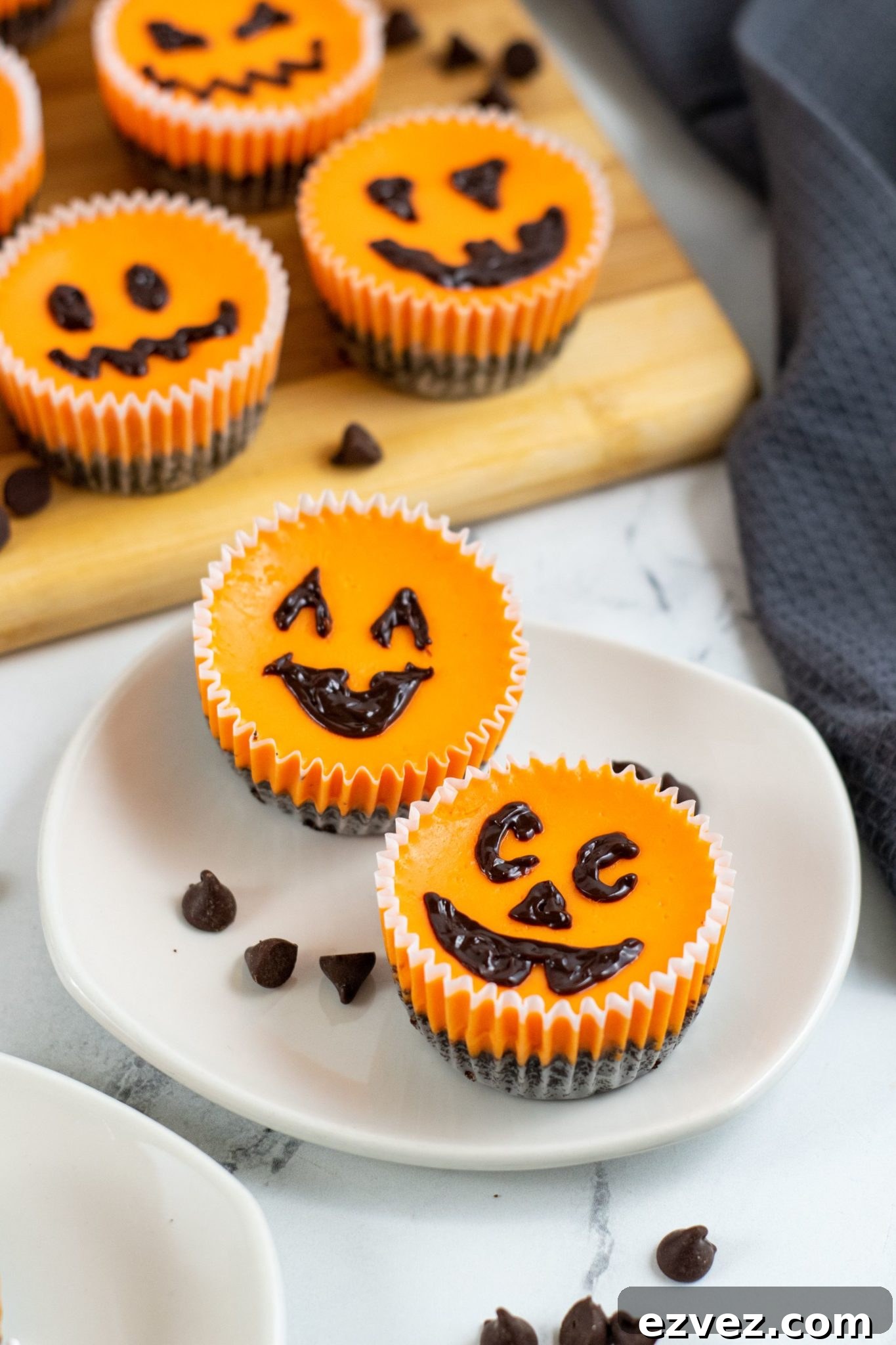Jack-o'-Lantern Halloween Cheesecake Recipe for Party Treats 2 Mini Halloween Cheesecakes on a white plate with jack o lantern faces.