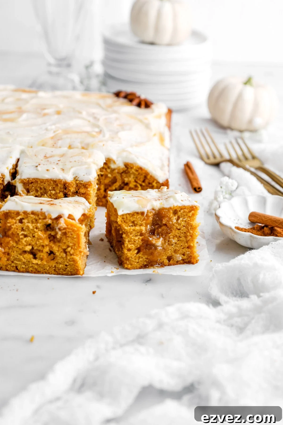 Pumpkin Caramel Poke Cake Recipe — Gooey Fall Dessert 2 pumpkin poke cake on parchment paper with cinnamon sticks, gold forks, and pumpkins around.