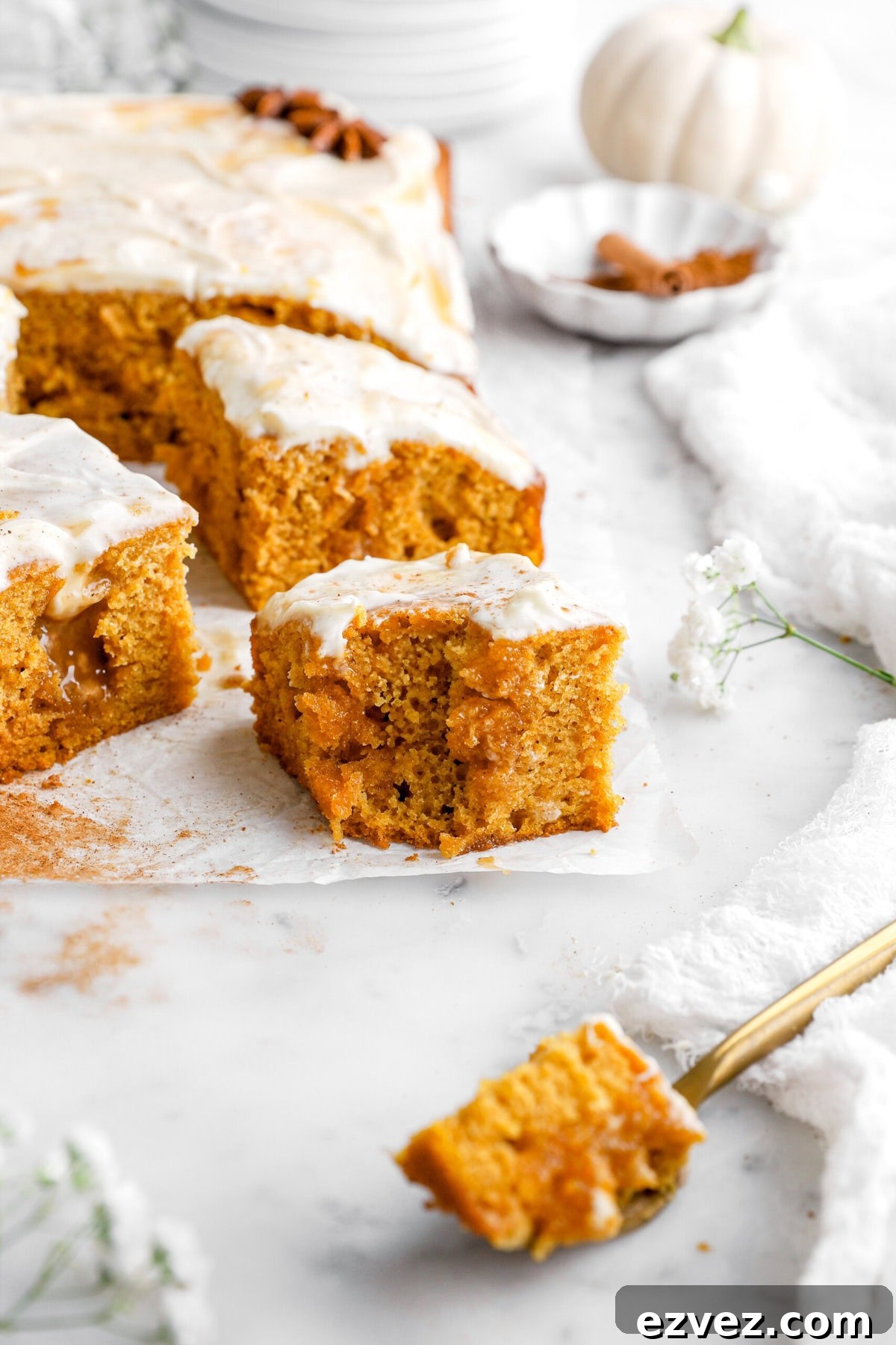 Pumpkin Caramel Poke Cake Recipe — Gooey Fall Dessert 3 bite of poke cake missing from slice on parchment paper.
