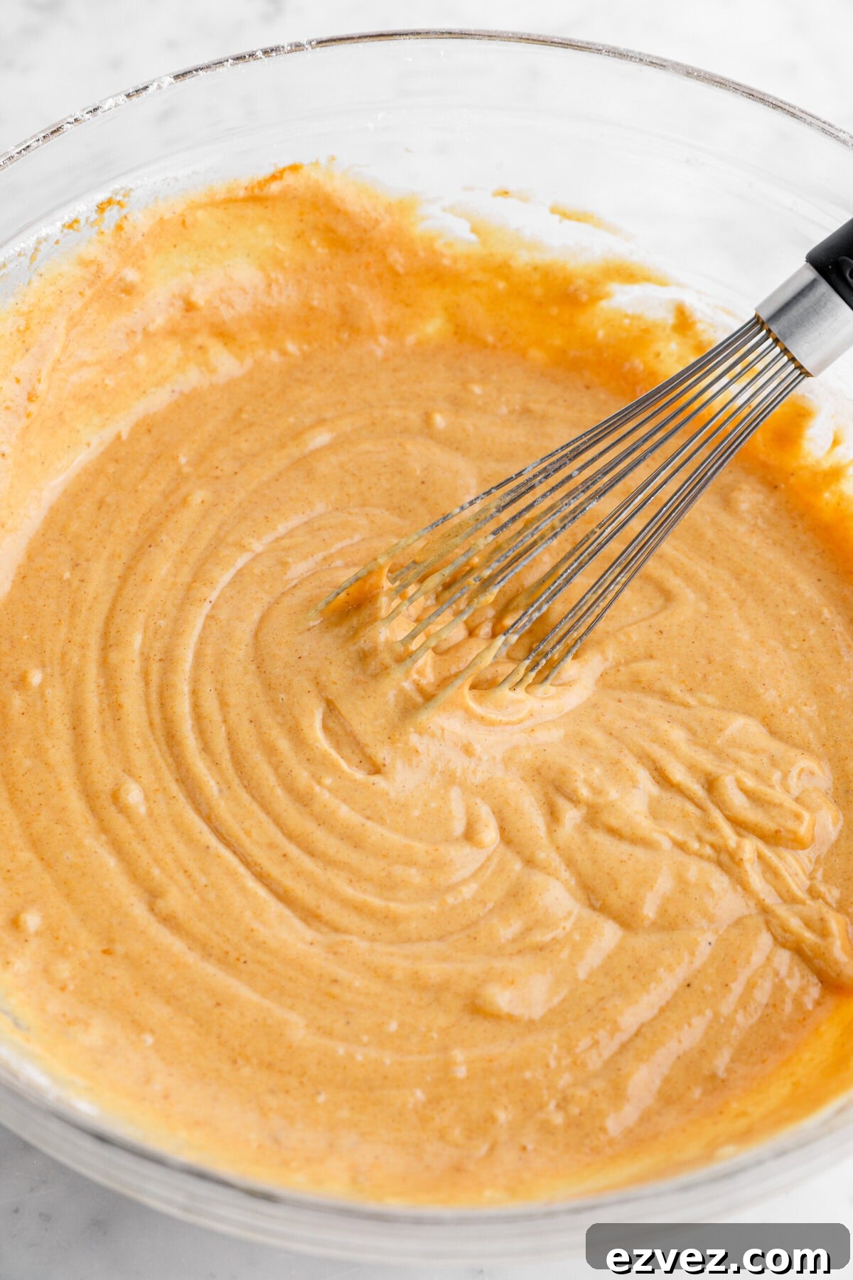 Pumpkin Caramel Poke Cake Recipe — Gooey Fall Dessert 4 pumpkin batter in glass bowl with whisk.