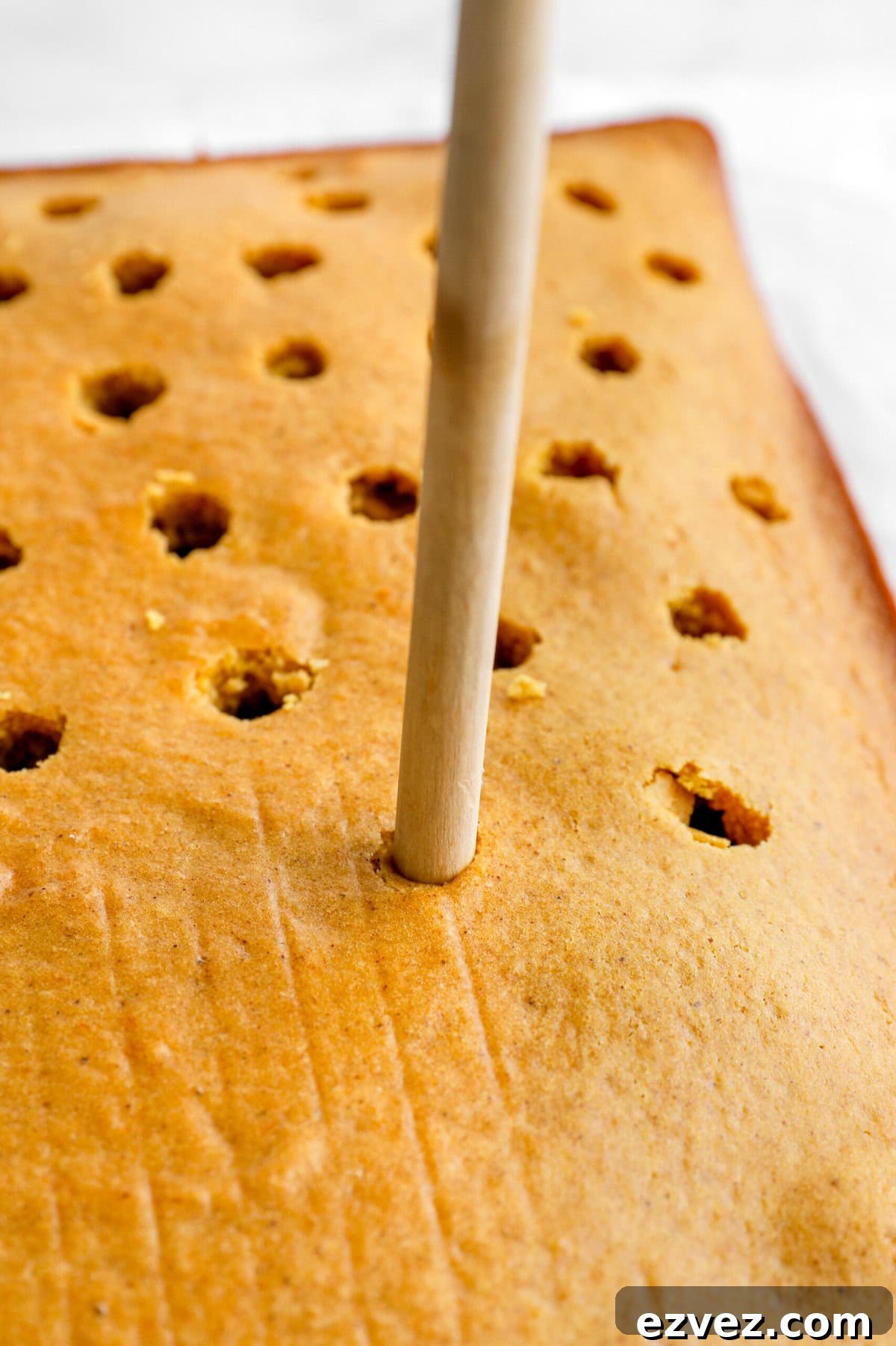 Pumpkin Caramel Poke Cake Recipe — Gooey Fall Dessert 6 wooden spoon handle poking holes into cake.