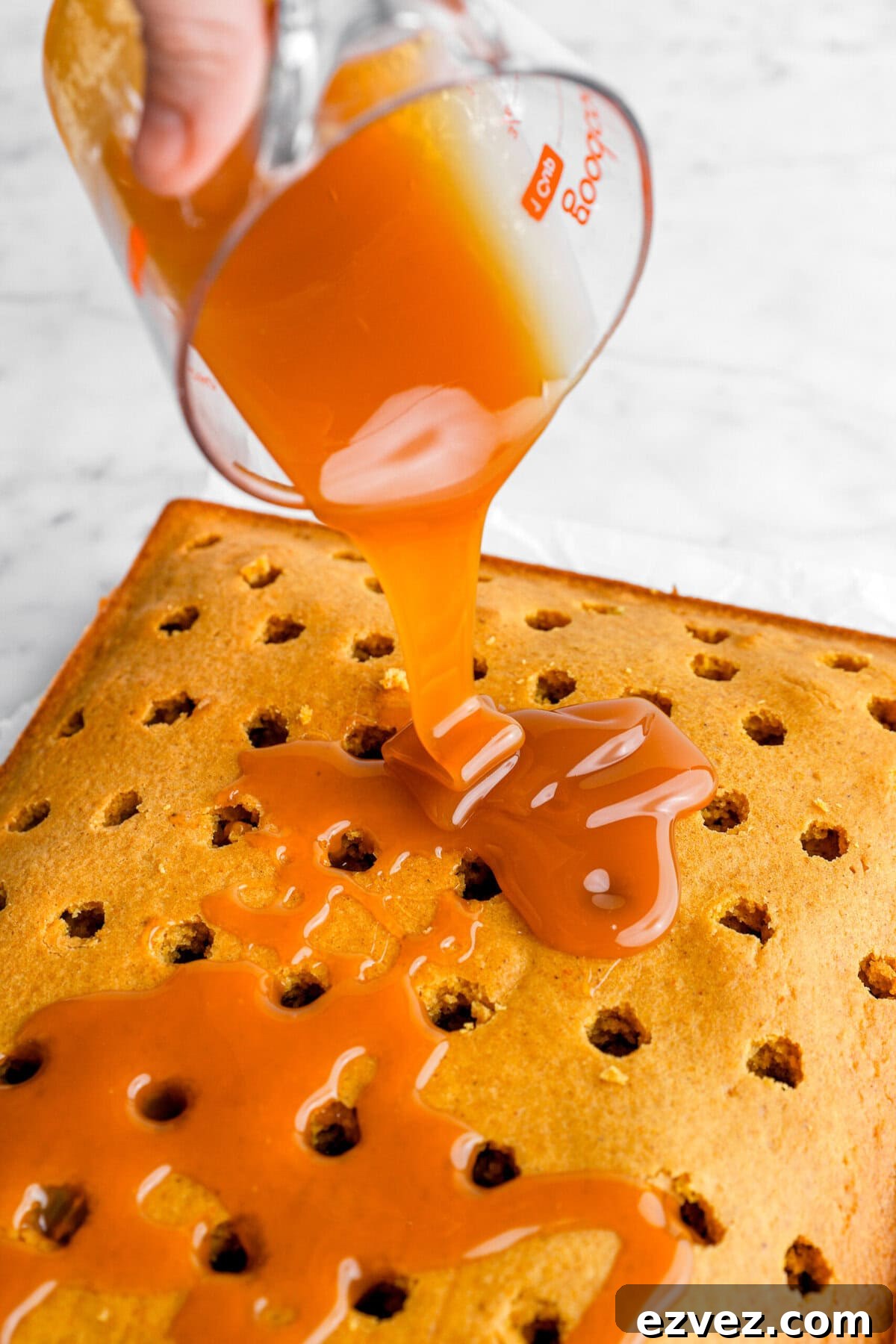Pumpkin Caramel Poke Cake Recipe — Gooey Fall Dessert 7 caramel being poured on top of cake.