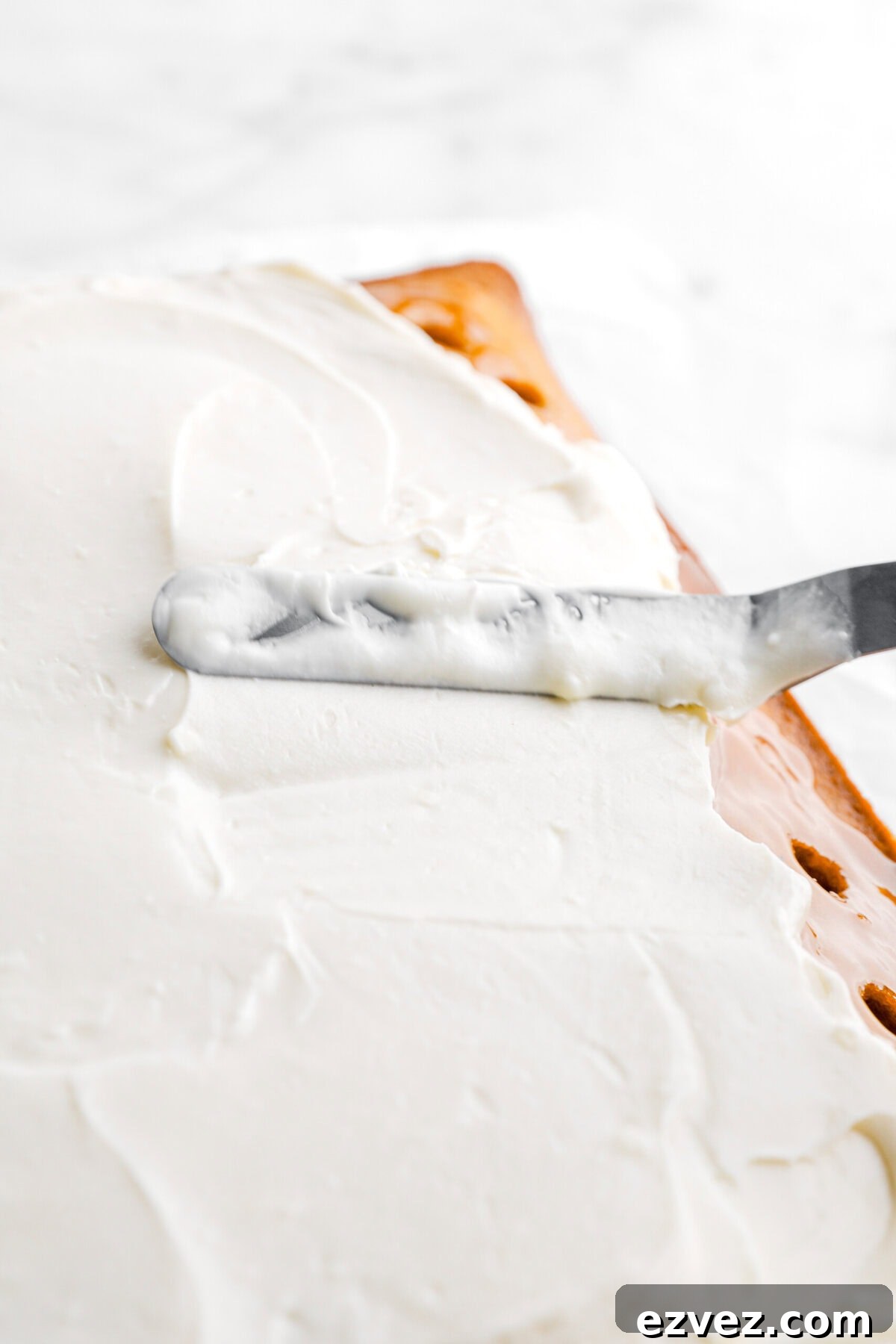 Pumpkin Caramel Poke Cake Recipe — Gooey Fall Dessert 8 frosting being spread on cake.