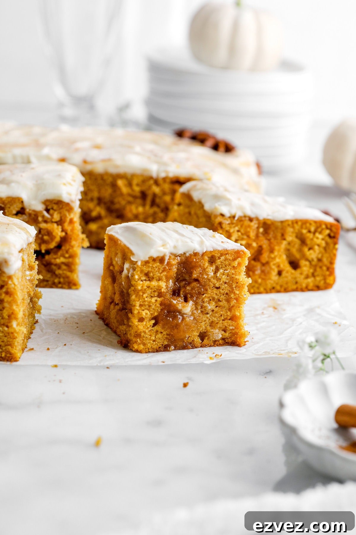 Pumpkin Caramel Poke Cake Recipe — Gooey Fall Dessert 9 pumpkin poke cake slice on parchment paper with slices of cake behind.