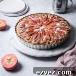 Pink Apple Tart with Cream Cheese Filling on a marble cake stand with a grey background; pink apples cut in half nearby