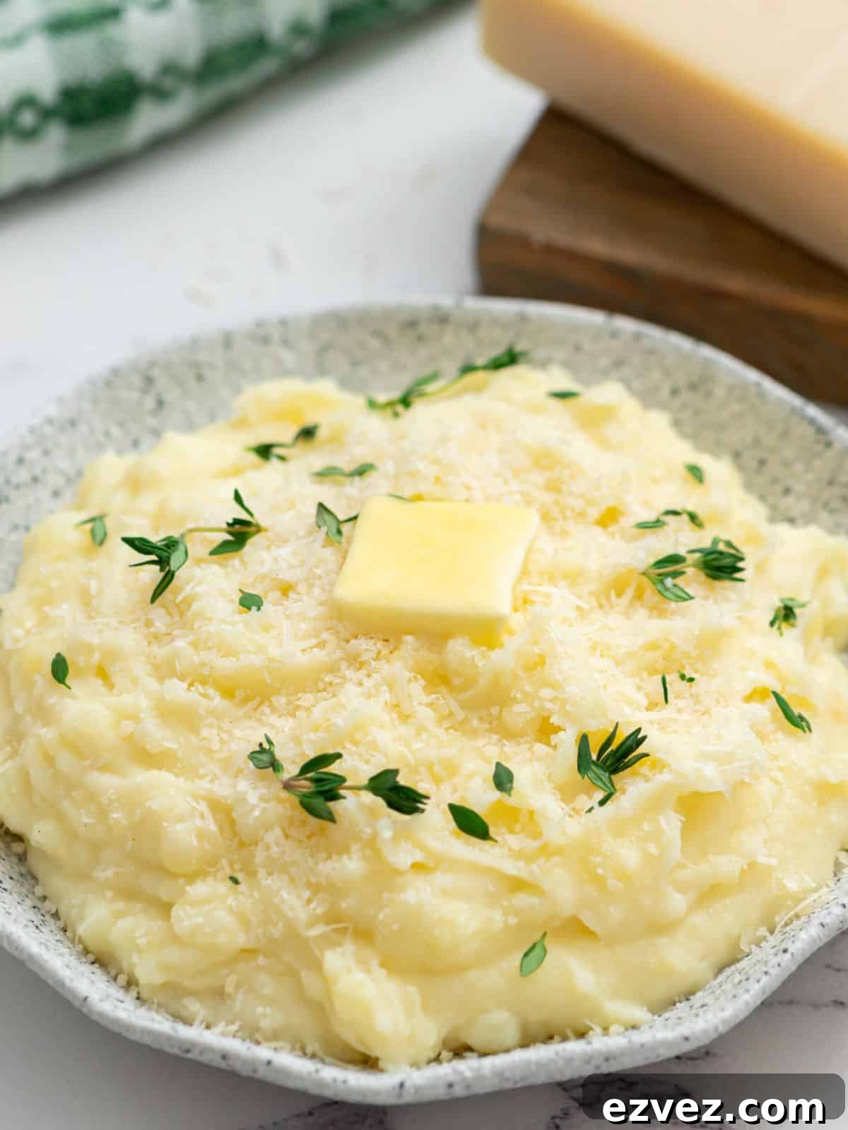 Crockpot mashed potatoes in serving bowl topped with parmesan, butter, and thyme.