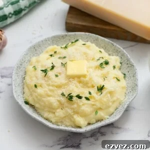Crockpot mashed potatoes in serving bowl topped with parmesan, butter, and thyme.