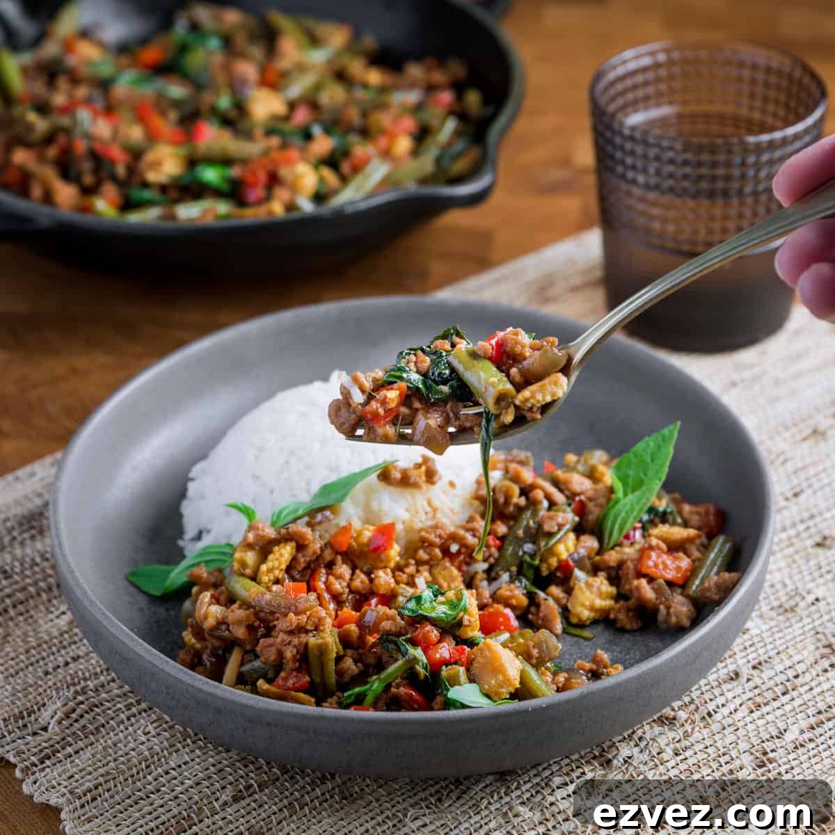 Photo of someone taking a forkful of thai basil vegan stir fry from a bowl of food with the pan in the background.