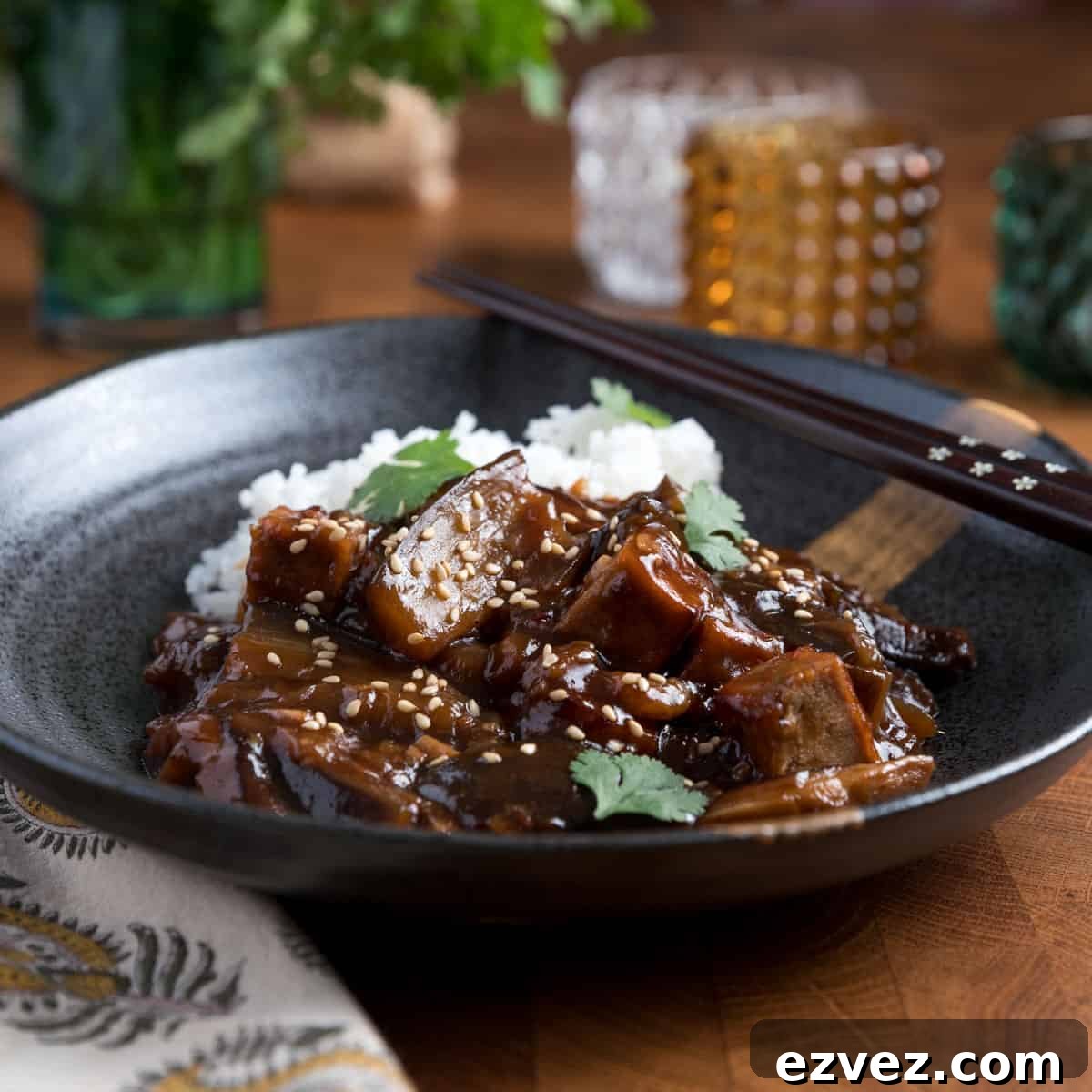 Photo of Chinese braised aubergine and tofu with rice in a black bowl with chopsticks.