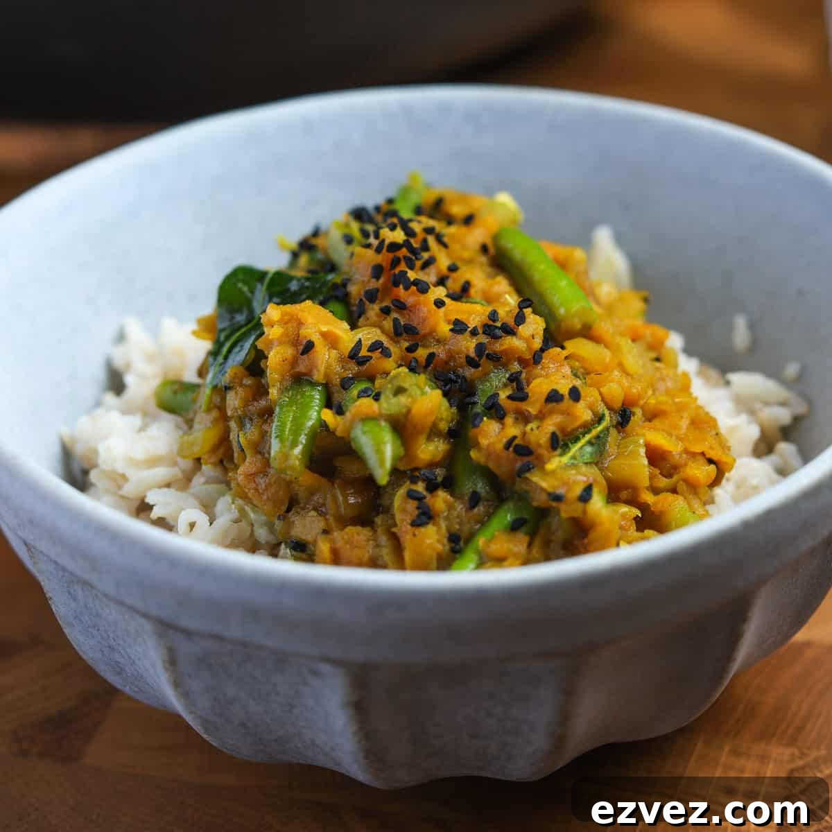 Photo of a blue bowl filled with pumpkin curry on a mound of brown rice, all on a wooden tabletop.