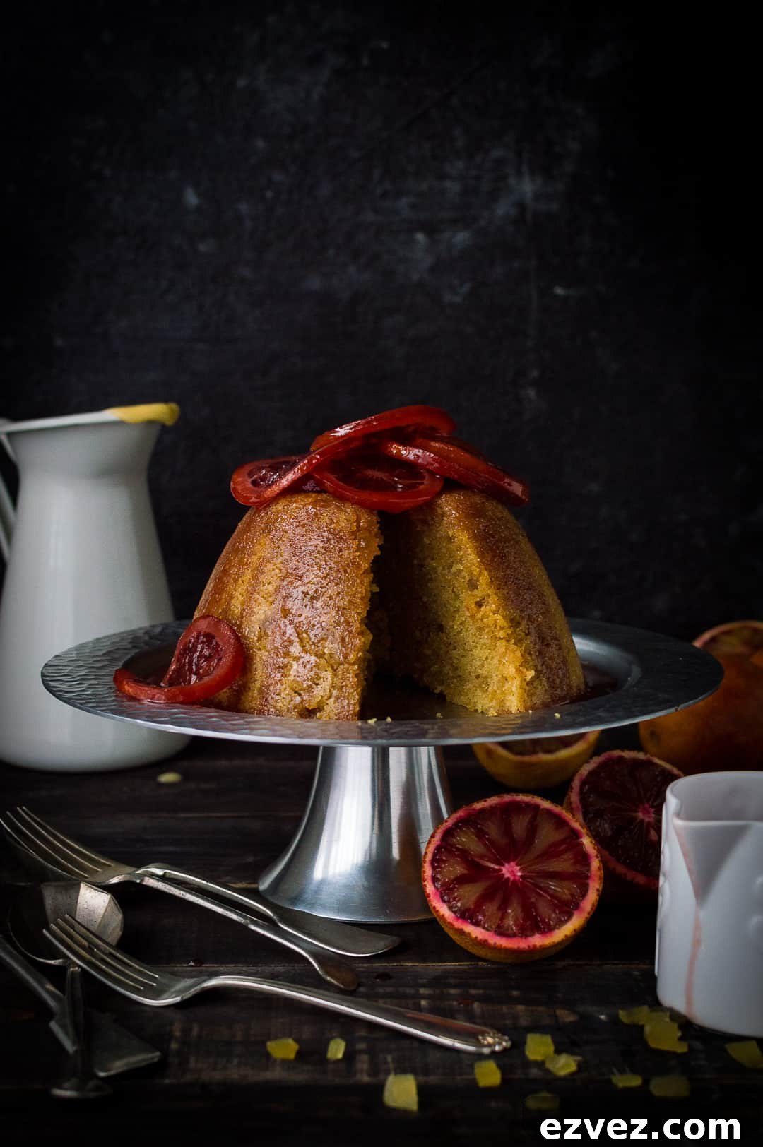 Sliced blood orange and ginger steamed pudding topped with candied blood orange slices on a silver cake stand
