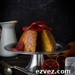 Sliced blood orange and ginger steamed pudding topped with candied blood orange slices on a silver cake stand