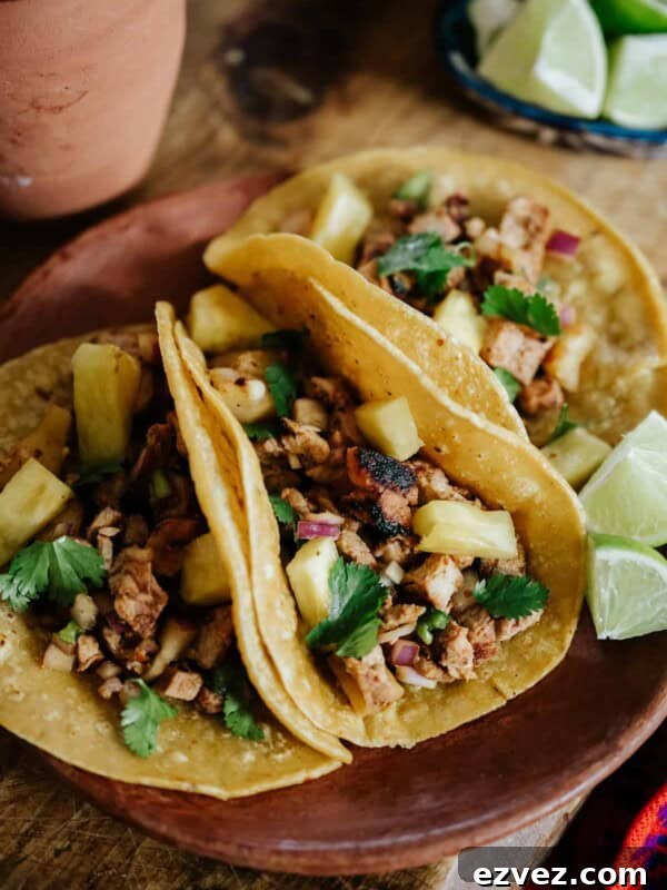 Colorado-Style Green Chile Pork Roast Recipe 13 Closeup of three grilled tacos al pastor filled with marinated pork and roasted pineapple on an earthenware plate.