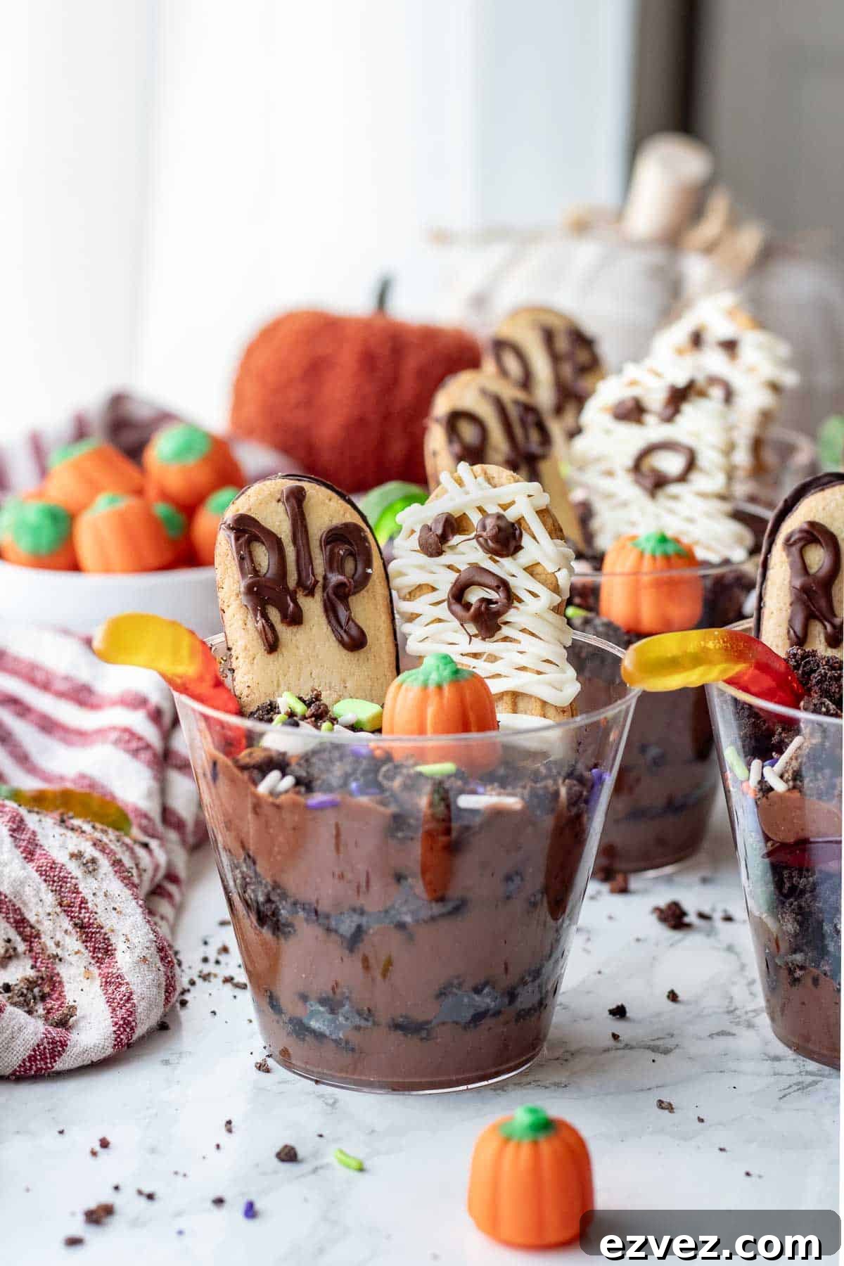 Spooky Halloween Pudding Cups Recipe for Party Treats 2 Clear cup of pudding and Oreos with worms, headstone cookie, and mummy cookie.