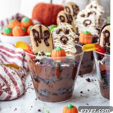 Spooky Halloween Pudding Cups Recipe for Party Treats 16 Clear cup of pudding and oreos with worms, pumpkin candy, sprinkles, headstone cookie, and mummy cookie.