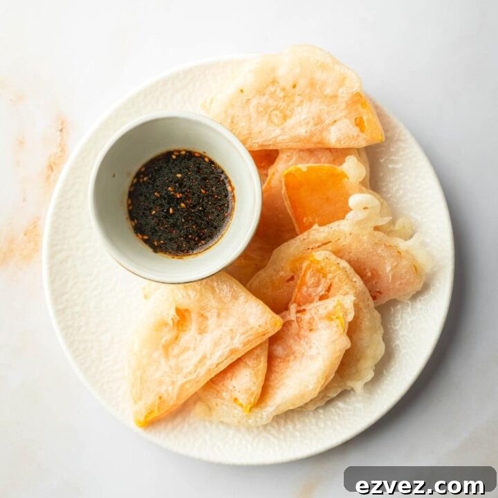 A bunch of pieces of fried squash overlapping one another. On the plate next to the squash is a bowl of soy sauce dipping sauce.