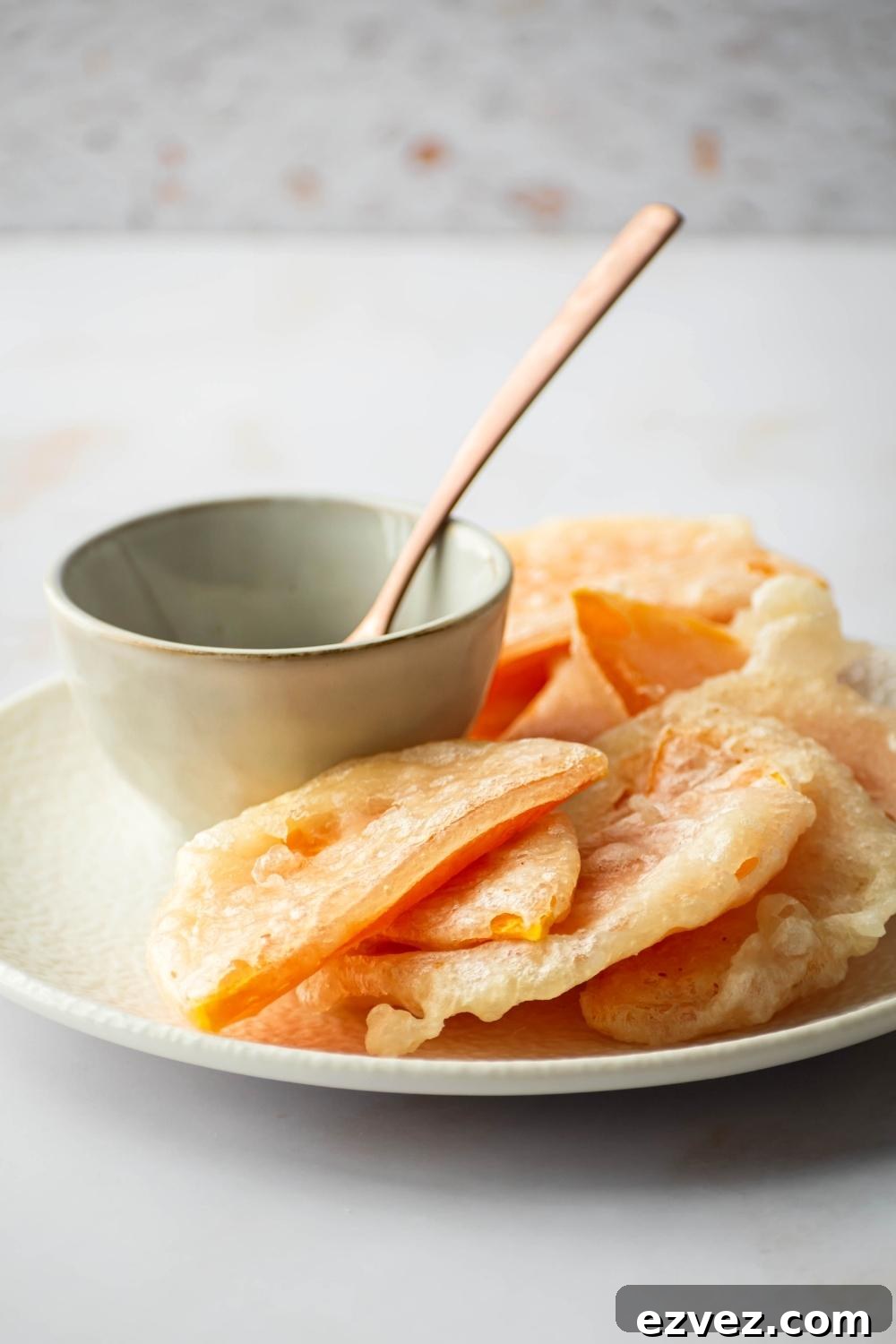 Crispy 4-Ingredient Fried Squash Recipe 3 A bunch of pieces of fried squash on a white plate with a bowl and a wooden spoon in it.