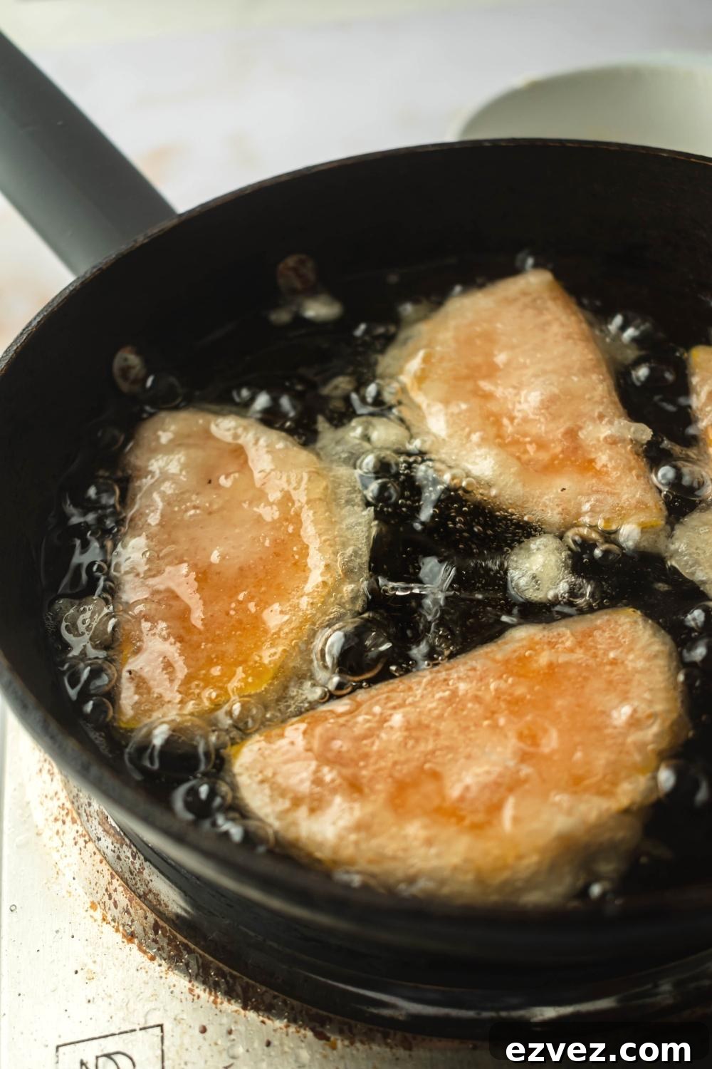 Crispy 4-Ingredient Fried Squash Recipe 7 Part of a frying pan with three pieces of squash submerged in oil.