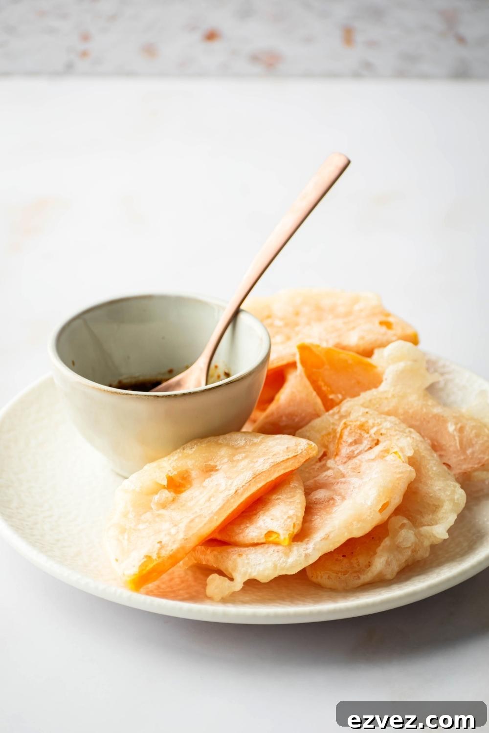 Crispy 4-Ingredient Fried Squash Recipe 9 Slices of fried squash overlapping one another on a white plate with a bottle of soy sauce with a wooden spoon in it next to the squash on the plate.