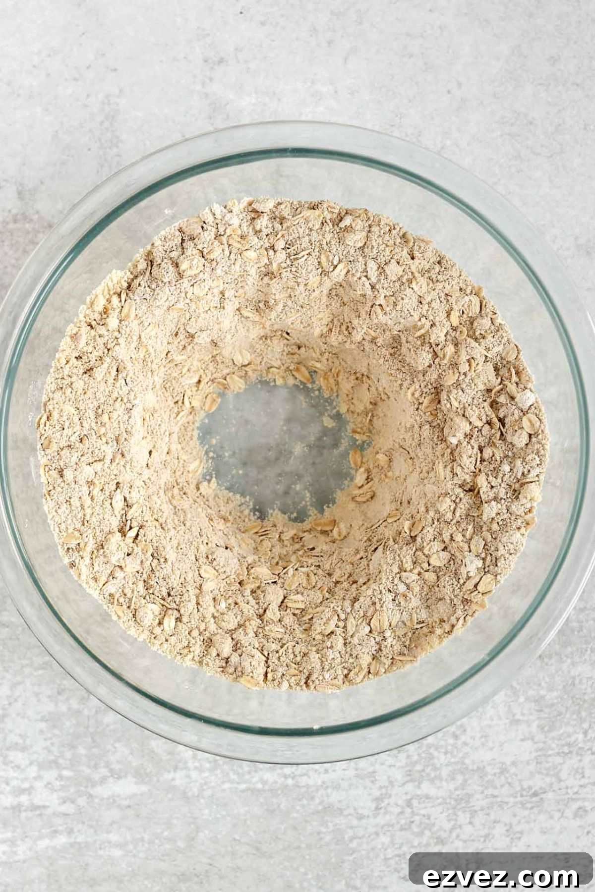 Dry ingredients for gluten-free banana muffins with a well in the center in a glass mixing bowl.