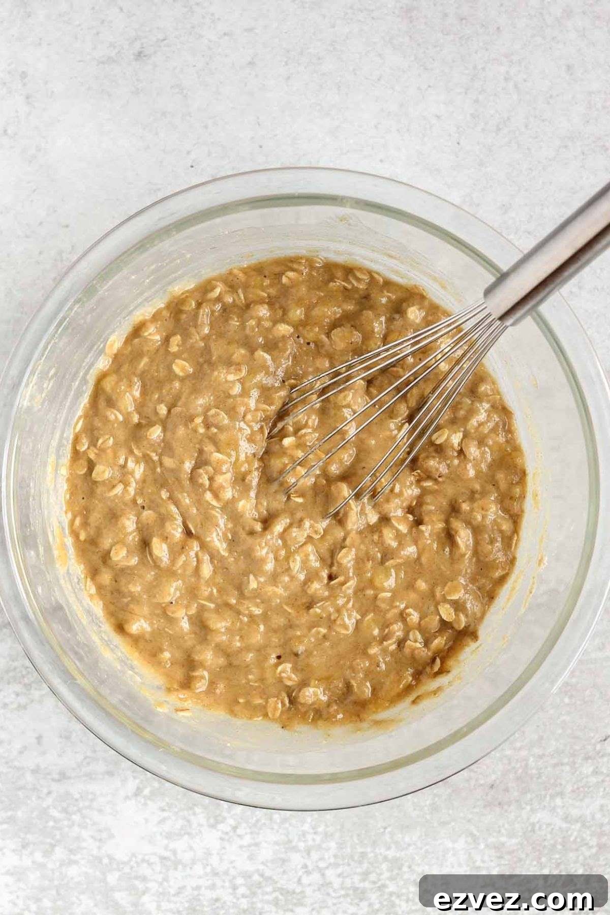 Banana muffin batter with a wire whisk in a glass mixing bowl.