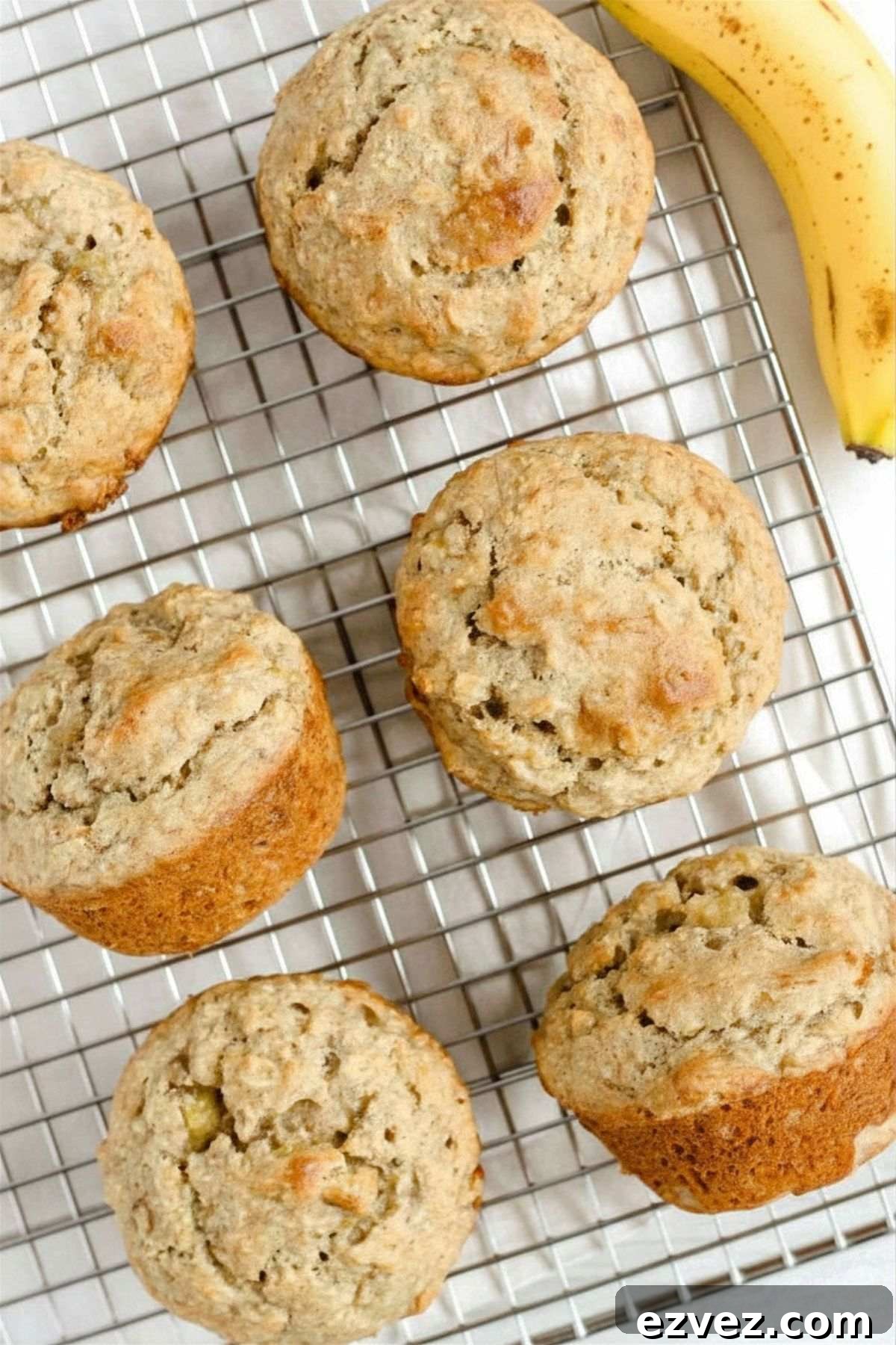 Banana oat muffins on a wire cooling rack with a banana on the side.