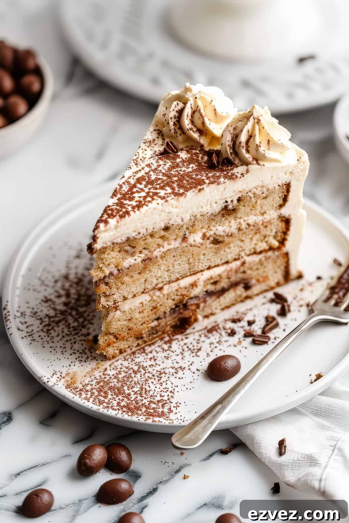 A slice of tiramisu layer cake with a fork and some coffee beans.
