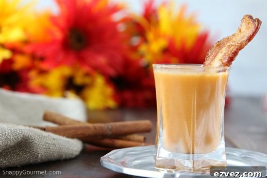 carrot soup shooter in shot glass with strip of bacon and cinnamon sticks in background with fall flowers