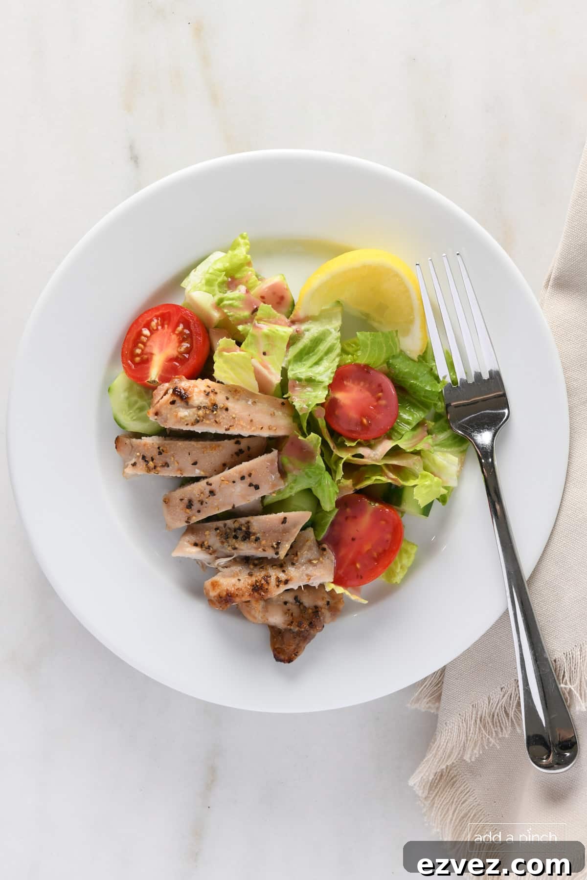 Sliced chicken thighs on a white plate with a garden salad and lemon wedge.
