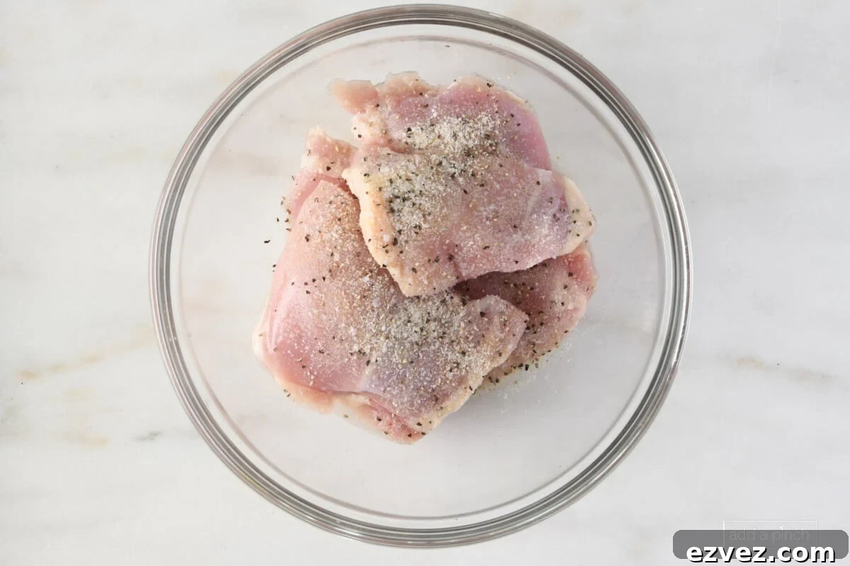 Chicken thighs marinating in a glass bowl on a marble surface.