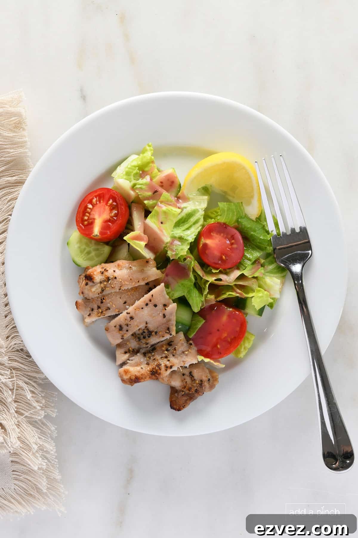 Chicken thighs on a white plate with a salad and lemon.