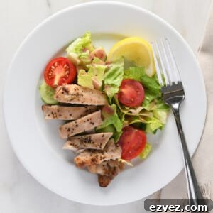 Sliced chicken thighs on a white plate with a garden salad and lemon wedge.
