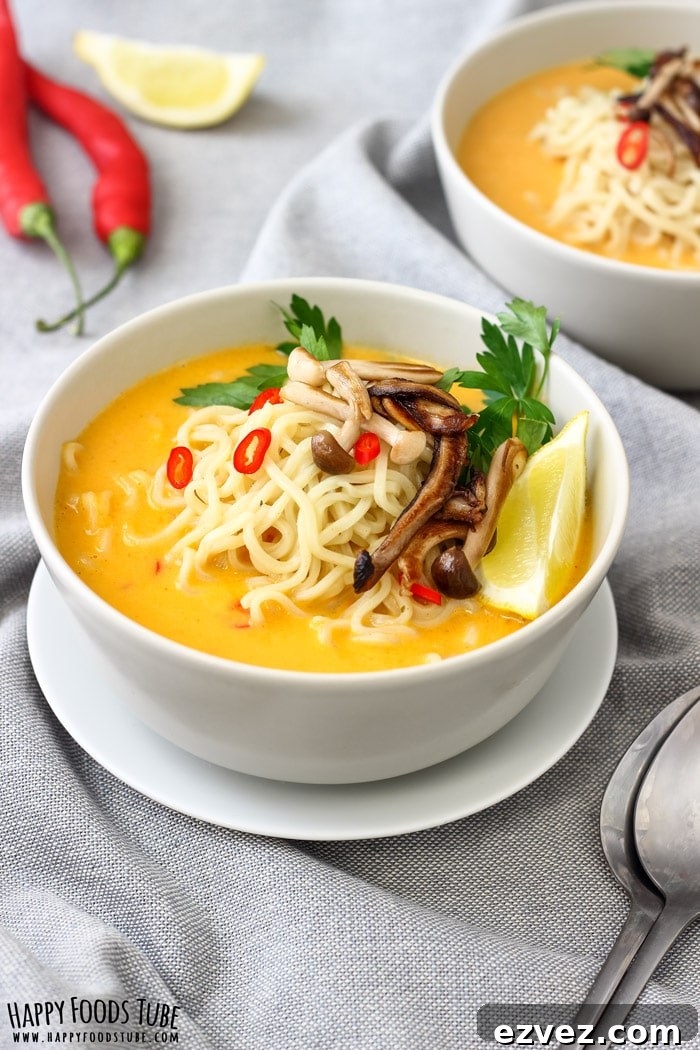 Thai pumpkin soup with coconut milk topped with ramen noodles, mushrooms and a lemon wedge in a bowl.