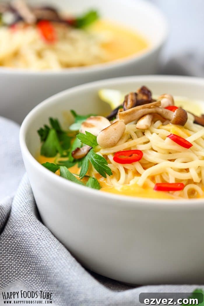 Side view of Thai pumpkin soup with noodles, parsley and red chili in a white bowl.