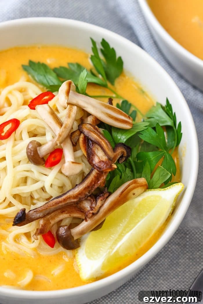 Close-up of ramen noodles and pan roasted mushrooms in creamy pumpkin coconut soup with a lemon wedge.