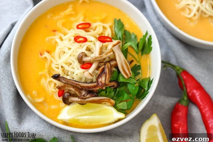 Overhead bowl of creamy pumpkin coconut soup with noodles, mushrooms, parsley and red chili slices.