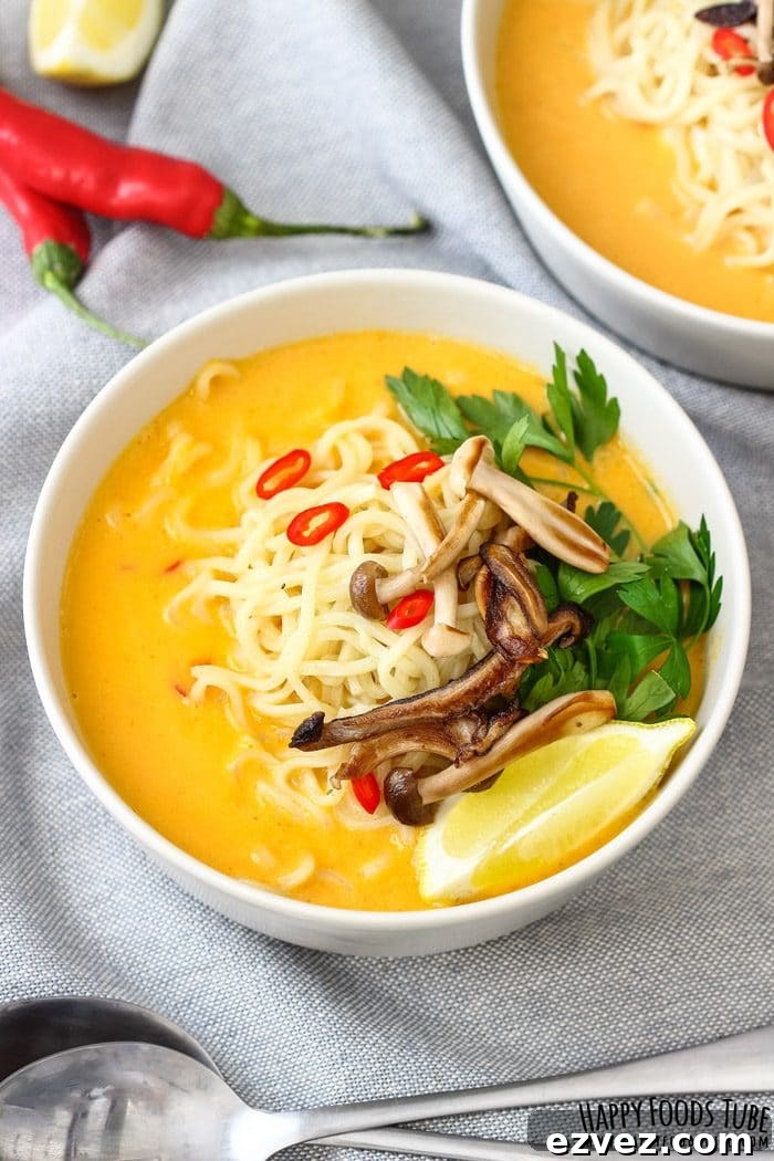 Two bowls of creamy pumpkin coconut soup with noodles, mushrooms, parsley and lemon wedges.