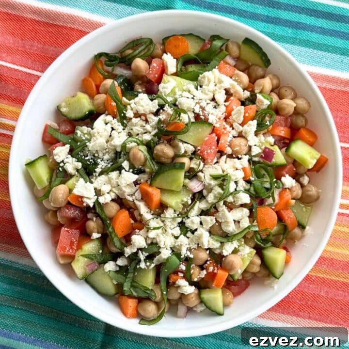 Chickpea feta cucumber salad with red onions, carrots, and tomatoes in a white bowl on a turquiose and orange cloth.