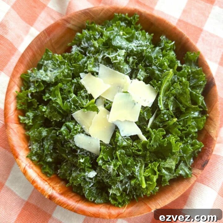Massaged kale salad topped with shaved Parmesan and lemon dressing in a brown bowl on a orange checkered background.