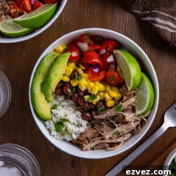 White bowl filled with pork carnitas, black beans, corn, salsa, garnished with lime slices and avocado wedges.