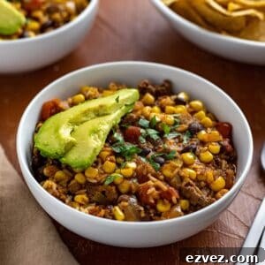 Cooked casserole in two white bowls with chips, avocado slices, lime wedges and spoons on the side.