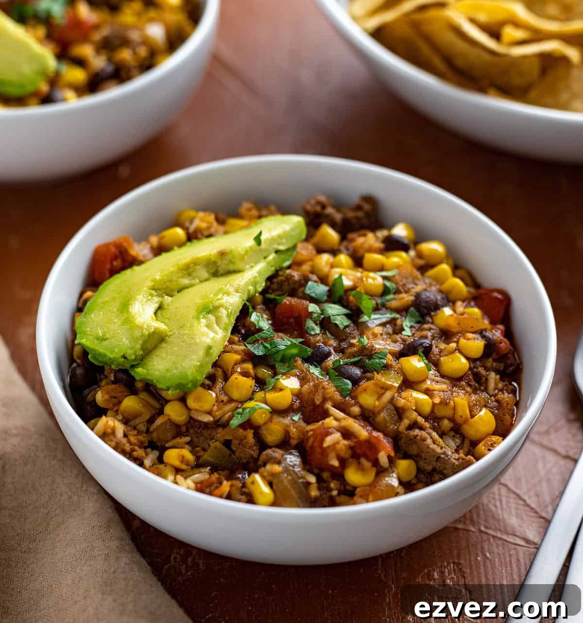 Mexican Casserole in two white bowls with chips, avocado slices, lime wedges and spoons on the side.