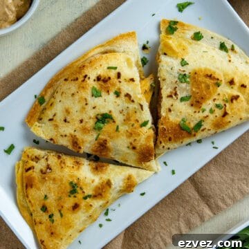 Three chicken quesadillas on white rectangular plate garnished with cilantro flakes.