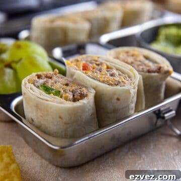 Taco meat pinwheels in a stainless steel meal prep container with guacamole and green grapes on the side.