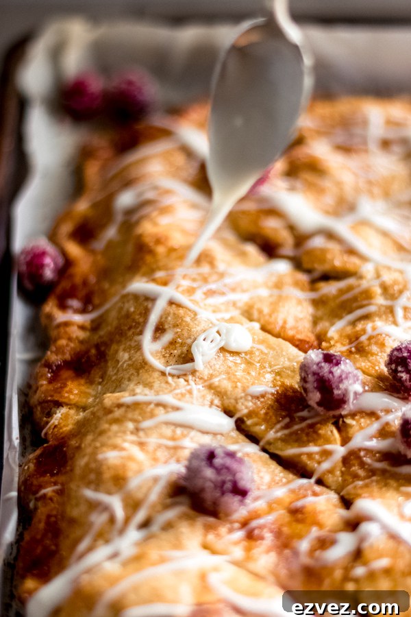 Spoon drizzling maple glaze over apple cranberry slab pie on a tray.