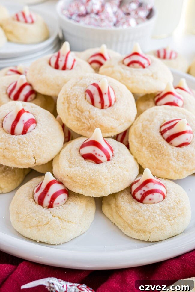 Overhead shot of Candy Cane Kiss Cookies piled on a white plate, showing the red and white peppermint Kisses.