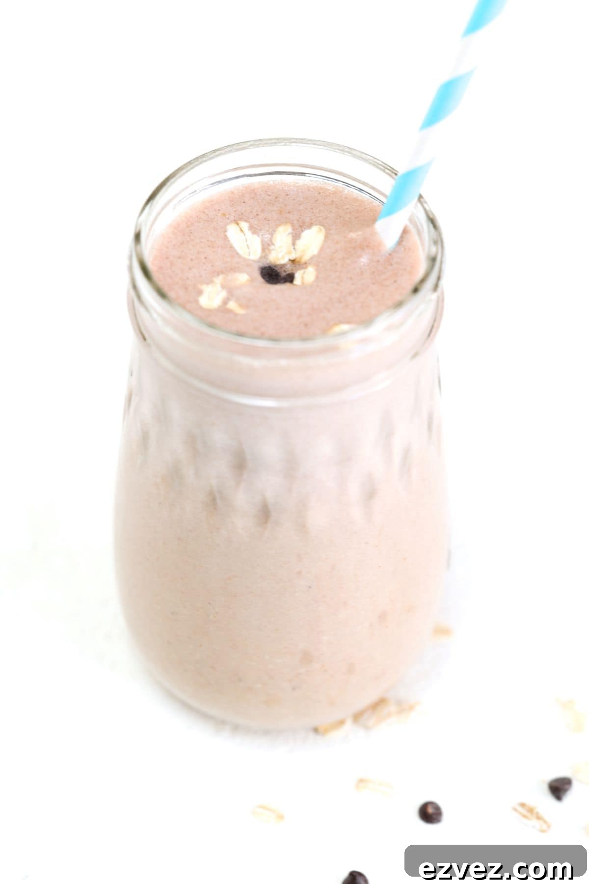 One peanut butter banana oatmeal smoothie in a glass jar with a blue and white striped straw.