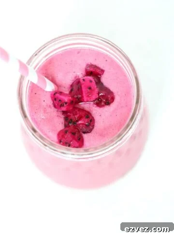 Top view of a pitaya smoothie in a glass jar topped with pieces of pitaya and a pink and white striped straw .